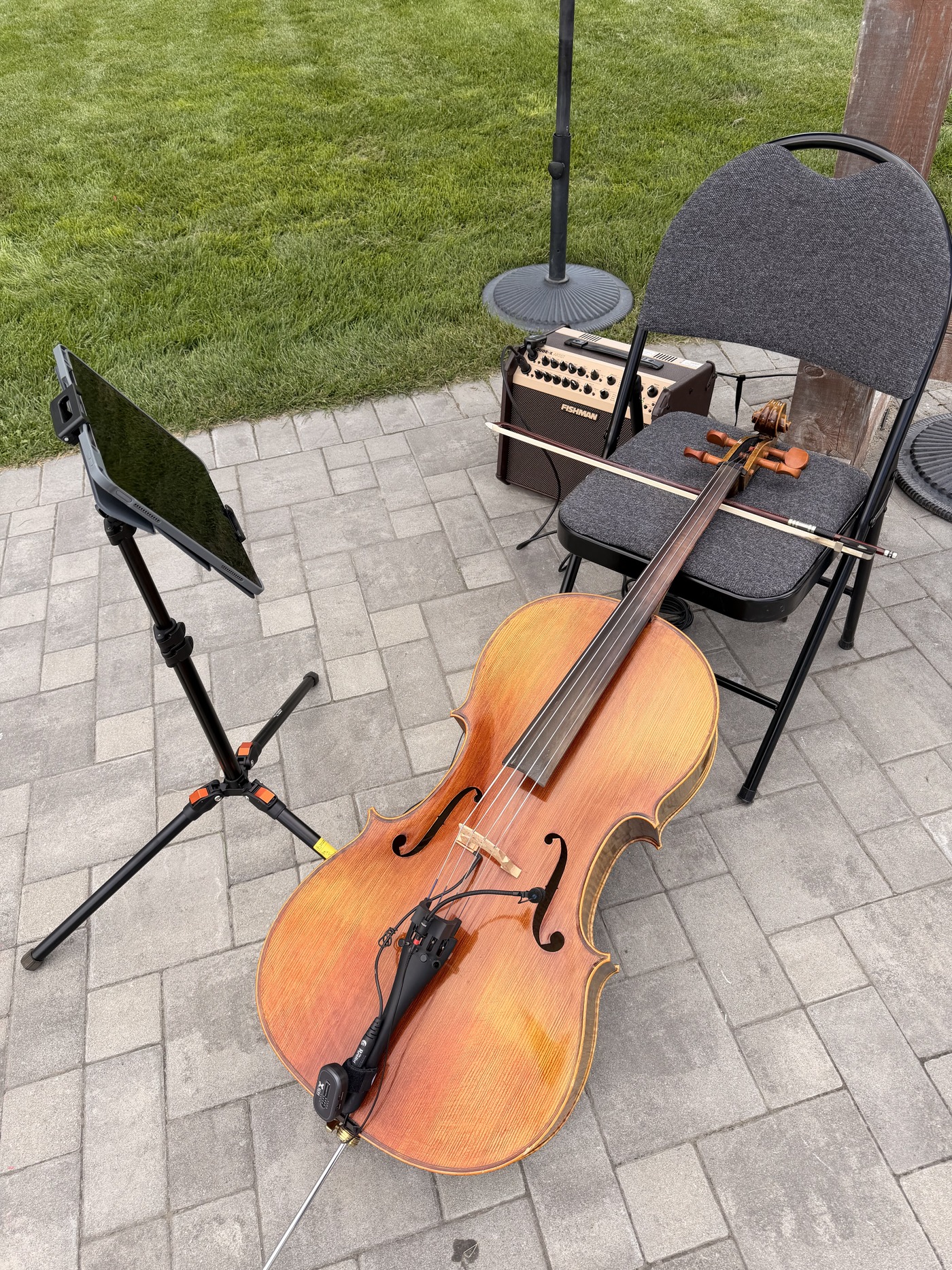 Yaroslav's cello, bow, amplifier and music stand set up on a patio outdoors